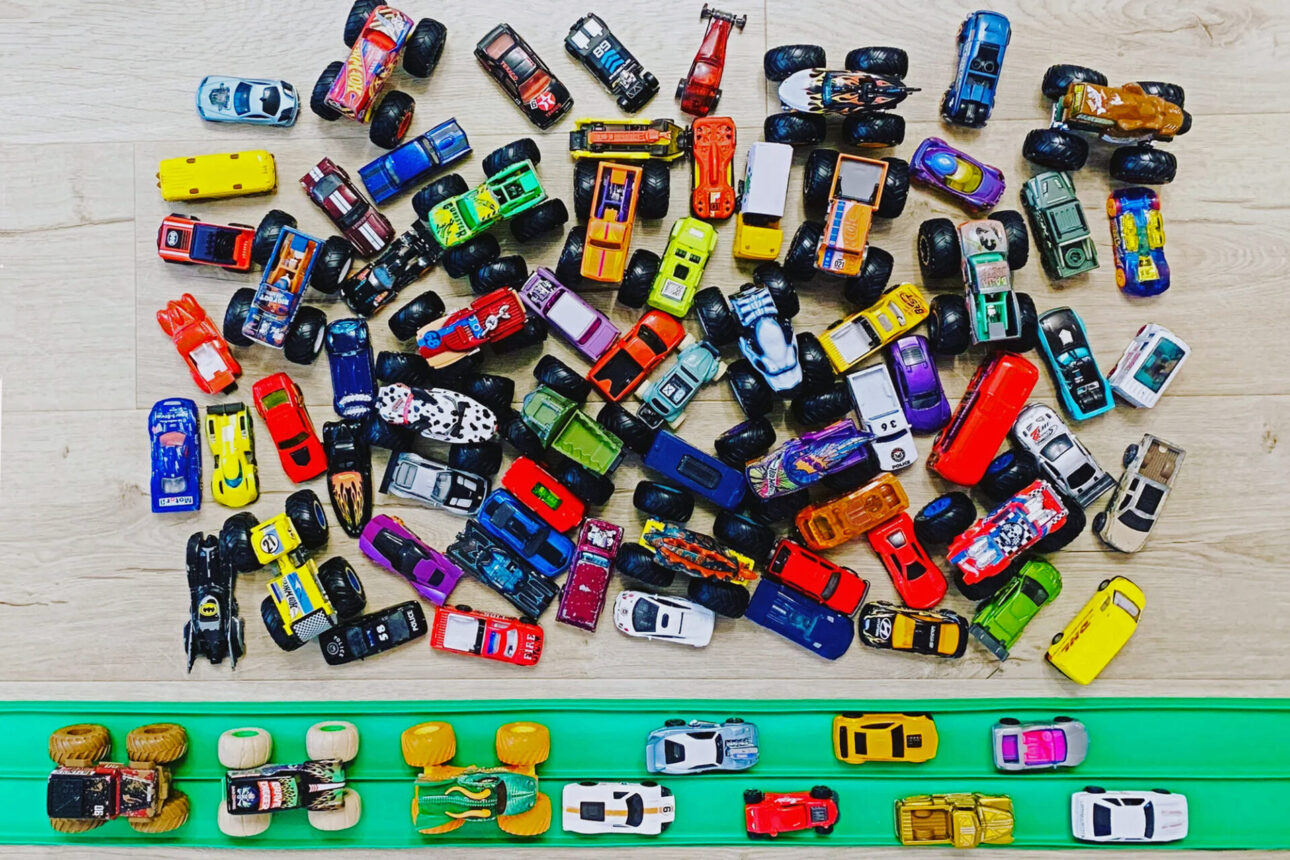 Lots of diecast toy cars and monster trucks by a green FlexiTrack