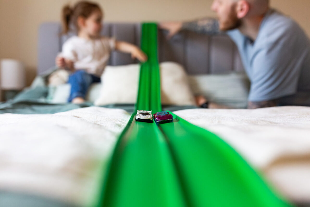 Dad and daughter racing toy cars along with a green FlexiTrack by Race Masters